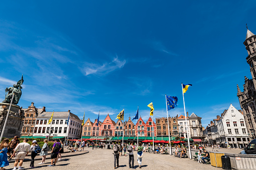 Bruges, Belgium. 16 July 2022. Flags fly in town square in Bruges with people walking on the street.