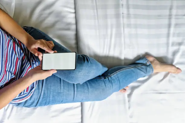 Overhead view of a woman using smartphone in bed at home.