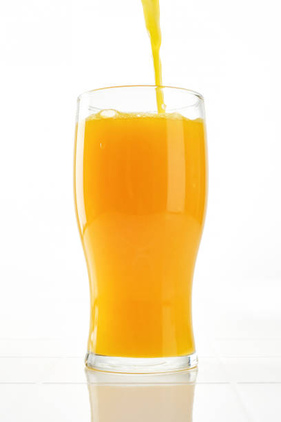 Orange Juice Pouring into Drinking Glass on White Background. Stream of Orange juice into a glass beaker. Shallow depth of field