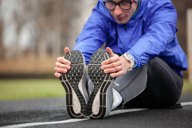 Shot of a young handsome professional runner stretching his feet. Young handsome professional runner stretching outdoors. hamstring injury stock pictures, royalty-free photos & images