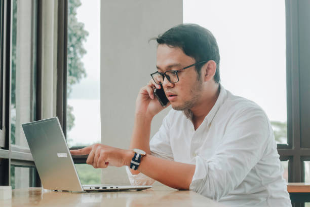 istock Young Asian businessman talking on a smartphone at a desk at caffe 1409906879