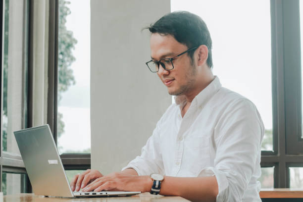 istock Young Asian man working on laptop computer while sitting at the cafe, looking through documents 1409909827