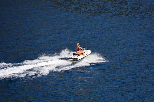 Marmaris, Turkey - July 2022: Woman in life vest and swimsuit rides a jet ski on the sea . Water sport in summer, riding a hydrocycle in the area of Marmaris town