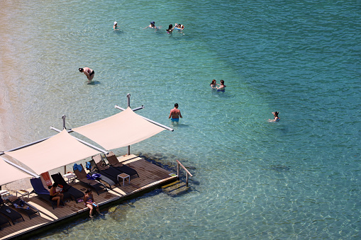 Turunc, Turkey - July 2022: People sunbathing and swimming in transparent water of Mediterranean sea on Turunc beach