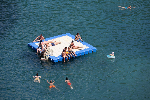 Turunc, Turkey - July 2022: People in swimwear sunbathing on floating pontoon in azure water of Mediterranean sea in the area of Turunc town