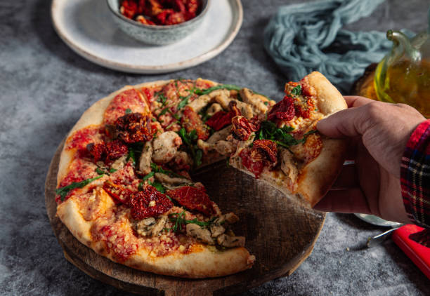 istock Man's hand holding a slice of delicious pizza on a rustic table, he is holding a slice. 1409911690