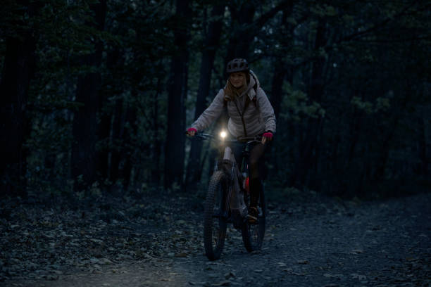 Young woman on a night e-bike ride Low-key photo of a cheerful young woman riding her enduro mountain bike (eMTB) at night, with a front light on. bicycle light photos stock pictures, royalty-free photos & images