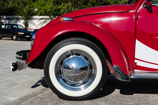 Praia Grande, São Paulo - Brazil - July 25, 2021: Old red Volkswagen Beetle customized with the Coca Cola brand. Chrome hubcaps and white tire strip.