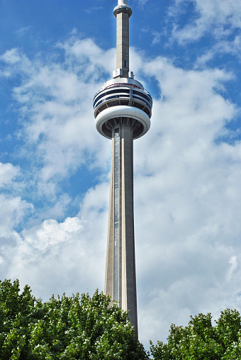 View of CN Tower from a park in Toronto, Canada. CN Tower against a blue sky with clouds in downtown Toronto, Ontario.