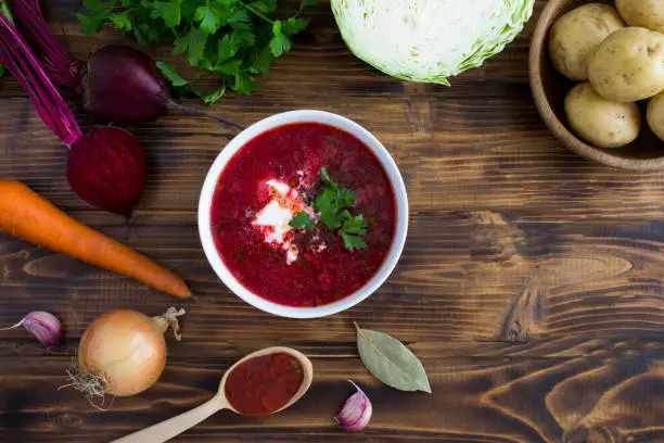 Top view of borsch in the white bowl and ingredient on the wooden background. Ukrainian food. Copy space. Close-up.