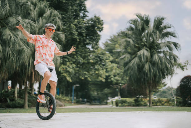 азиатский китайский зрелый мужчина, практикующий одноколесный велосипед в общественном парке - unicycle стоковые фото и изображения