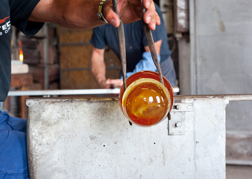 Couple of glass blowers are modeling melting glass using pliers and rotation.