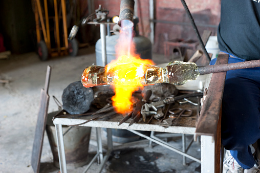 Craftsman needs to reheat the glass during the creative process of forging it. Here a powerful flame is used on a piece of glass stuck to a blowing barrel.