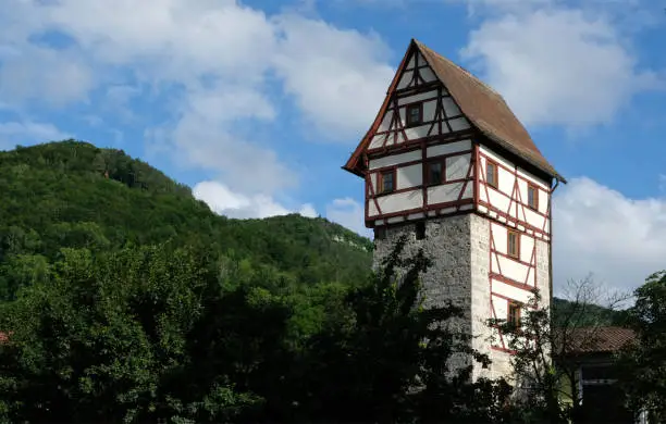A quaint medieval timber-framed tower in the town of Bad Urach, Germany, with a background of lush green forest under a blue sky