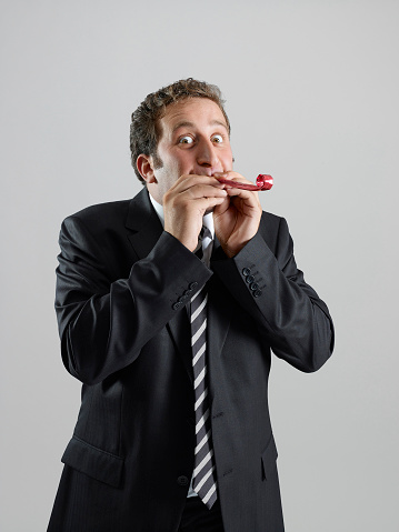 Businessman blowing a party horn blower in front fo a white background