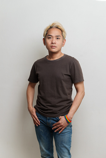 Studio portrait photo of young Asian man wearing rainbow wristband on white background. Young man emotion face expression portrait concept.