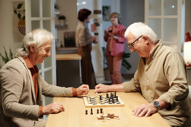 istock Two cheerful retired men in casualwear looking at chessboard with figures 1409921470