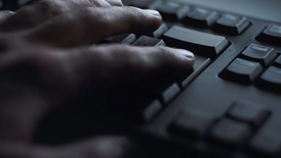 Close-up man presses keyboard key. Man presses button enter computer keyboard. Man's hand presses keyboard in light of computer screen.