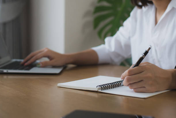 istock woman sitting at a desk with laptop and taking notes in a notebook. 1409923715
