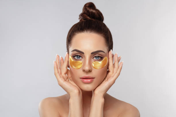 Beauty model girl face with healthy fresh skin. Woman with under eye collagen gold pads.  Skin care concept, anti-aging moisturizing eye mask, golden hydrogel patches, eye skin treatment, cosmetology. stock photo
