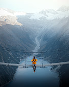 istock Man in yellow jacket sitting on a suspension bridge over a lake in Olpererhutte, Austria 1409931022