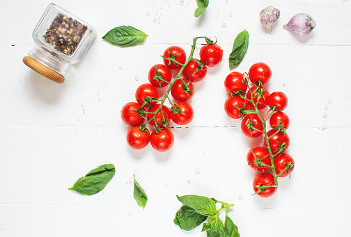 Fresh cherry tomatoes and basil with spices on a white wooden background . Top view