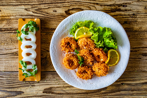 Fried breaded calamari rings with lemon and lettuce on wooden table
