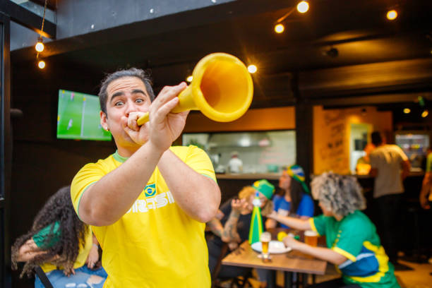 portrait of brazilian man playing vuvuzela, in front of a group of brazilian friends, watching game in a bar group of brazilian friends watching game at a bar vuvuzela stock pictures, royalty-free photos & images