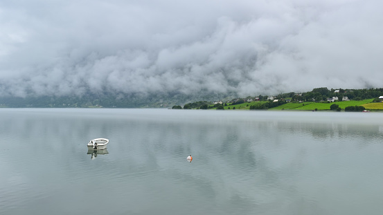 Small boat and buoy in fjord water on a misty day, green shore shrouded in white stormy clouds, Norway, Scandinavia, Europe