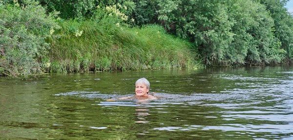 Senior happy woman swimming in a calm river in the countryside. Country life concept Banner