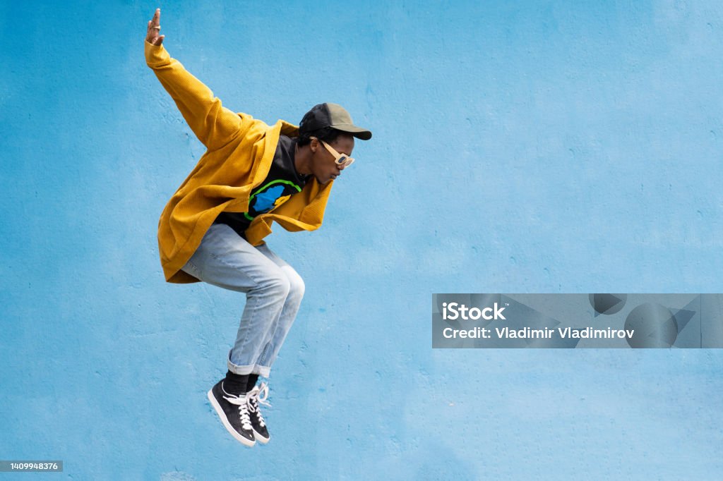 Man doing contemporary modern dance move Man dressed in street style clothing is coming downwards after jumping high in the air against blue background Jumping Stock Photo