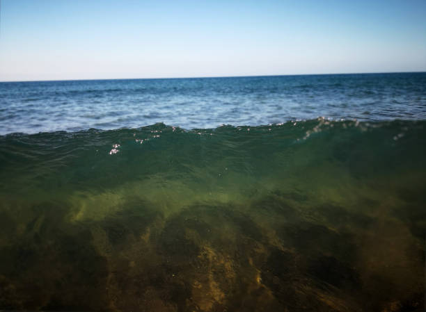 Green transparent water of the Atlantic ocean with blurry sand illuminated by sunlight under it seen through the water and blue surface of the water edge at the beach of Lanzarote, Canary islands. The raised mass of water highlights the force of the wave Water mixing the sand with its motion creates the original. Beauty and the power of the nature bottom the weaver stock pictures, royalty-free photos & images