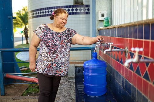 Portrait of a happy mature Latin woman drawing water from a natural source of water, in a small town. She has a water gallon with her to fill up with water at the mine.