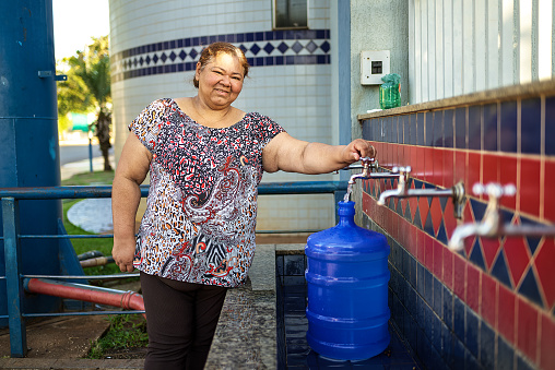 Portrait of a happy mature Latin woman drawing water from a natural source of water, in a small town. She has a water gallon with her to fill up with water at the mine.