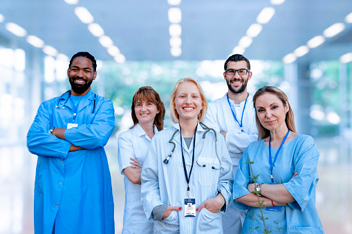 Diverse group of Doctors and nurses in Hospital clinic. Smiling friendly Health care workers looking at camera while standing in bright modern corridor.