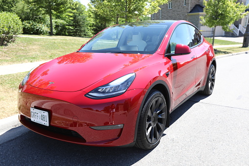 June 28, 2022 - Vaughan, Ontario, Canada: Front view of a brand new 2022 Tesla Model Y Dual Motor in red color with white and black interior. Modern electric vehicle. Environmentally-friendly car. Luxury electric crossover. Luxury electric SUV. Saving the planet by driving an electric vehicle. Modern and sleek car interior. Simple and beautiful design. Luxury vehicle.