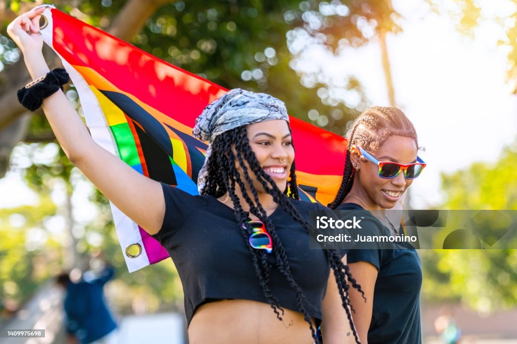 Afro-latinx young lesbians holding a rainbow banner with the word Proud written on it 18-19 Years Stock Photo