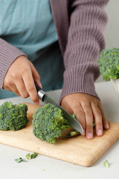 istock Female Cut Broccoli on Wooden Chopping Board 1409976324