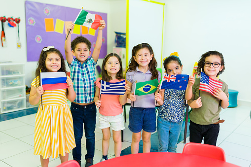 Diverse group of kindergarten children holding their country flags while learning geography and different cultures in preschool