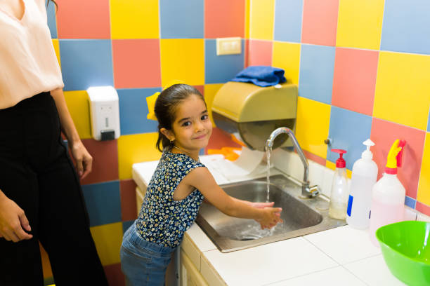 Cute kid going to the bathroom and washing her hands Portrait of a little girl student smiling while washing her hands after going to the bathroom in preschool teacher classroom child education stock pictures, royalty-free photos & images