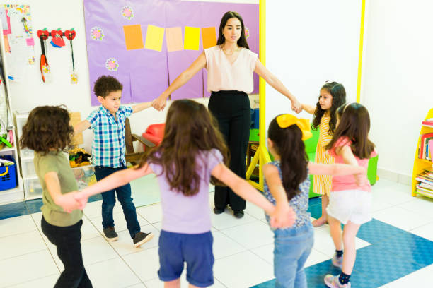 istock Cheerful playful teacher holding hands in a circle with her students 1409982133