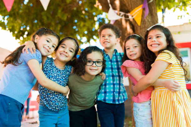 Cheerful preschool kids playing after school Fun caucasian and latin children hugging and laughing while playing outside in the kindergarten mexican  children stock pictures, royalty-free photos & images