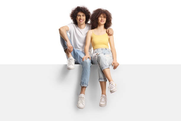 istock Young man and woman with curly hair smiling sitting on a blank panel 1409985040
