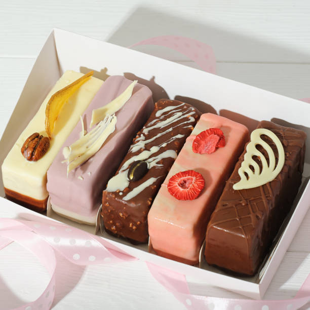 set of various mini cakes in a box with festive decor unboxed. glazed with chocolate and icing and berry filled cakes for present or sweet treat.