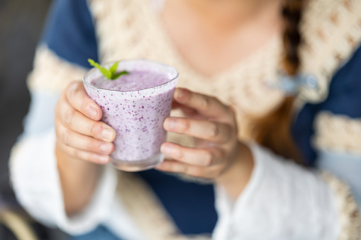 A close up of womans hands holding a blueberry smoothie drink.