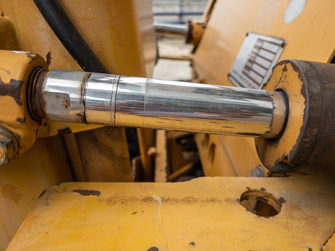 Closeup of the hydraulic cylinder with the oil stain of the small bulldozer on the construction site, front view for the copy space.