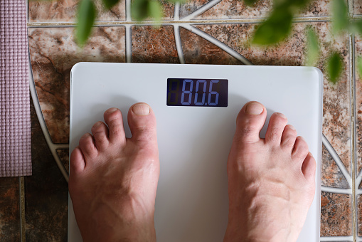Overweight man in bathroom stands with electronic weight meter. Weight loss concept