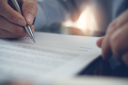 Businessman with pen in hand reading official business contract, rental agreement before making a deal. Man project manager signing document in office, close up.