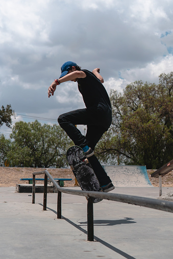 Skater dressed in black on his skateboard performing a trick on a tube in the park. It's a sunny day . There is free space for text