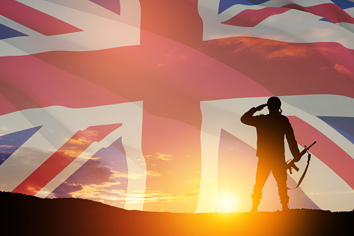 Silhouette of soldier with print of sunset saluting on a background of United Kingdom flag. Greeting card for Poppy Day, Remembrance Day. United Kingdom celebration.